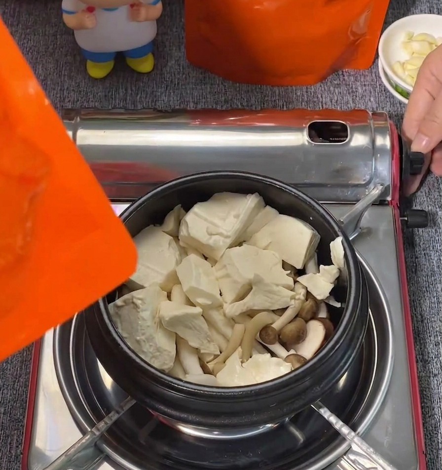 Bloques grandes de tofu blando blanco y hongos shimeji organizados en una olla negra.