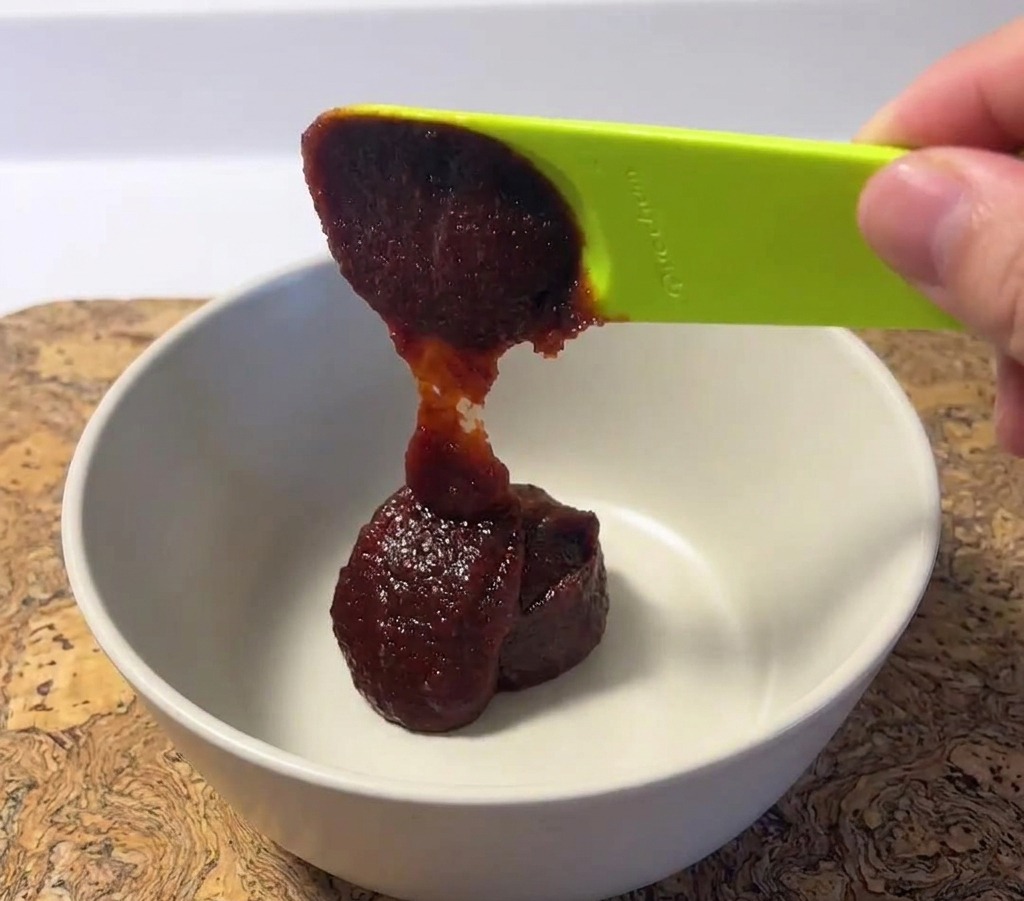 Una cucharada de pasta de chile rojo coreano espesa colocada en un bol de mezcla de cerámica blanca con una cuchara verde