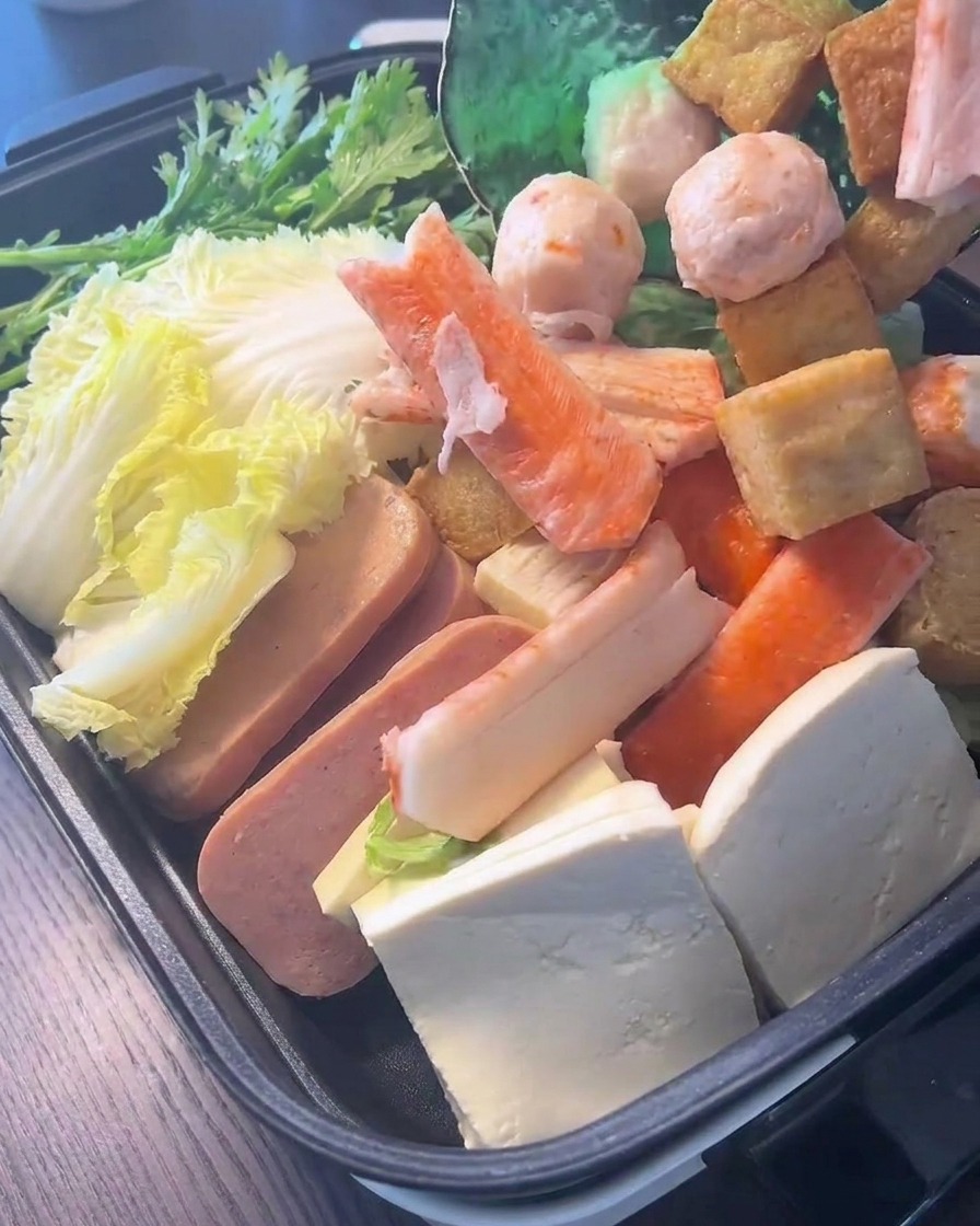 Una variedad de bolas de pescado y palitos de cangrejo que se agregan sobre hojas verdes frescas y repollo en la olla.