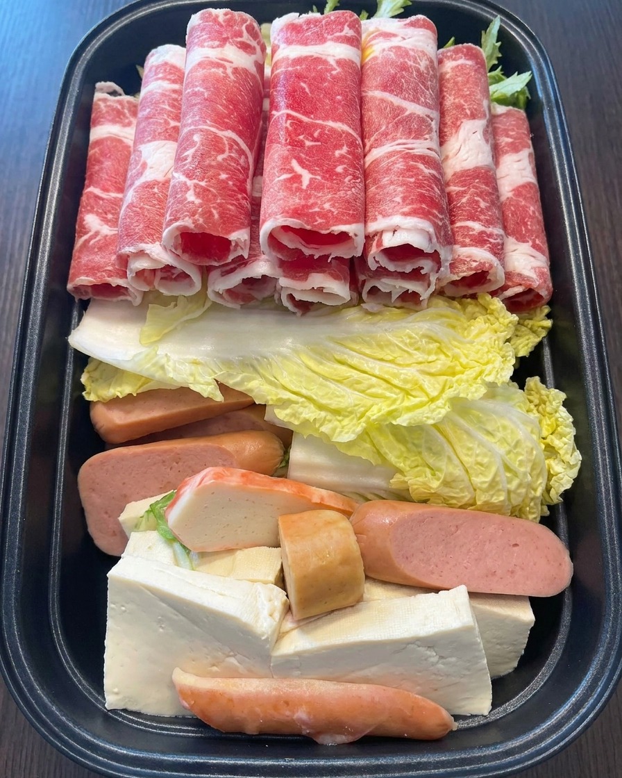 Una mano colocando varios rollos de carne de res finamente cortada sobre los ingredientes coloridos de la olla.