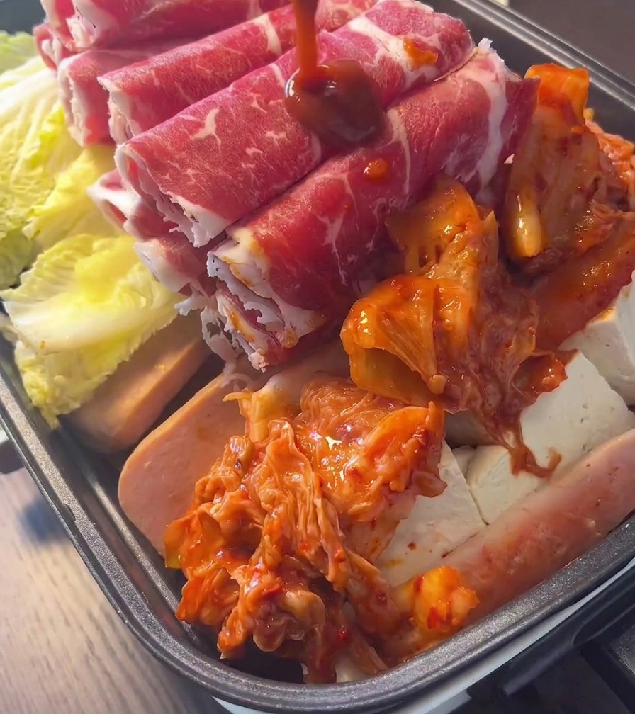Una pila de kimchi rojo brillante y fermentado en el centro de una olla llena de carne y verduras.
