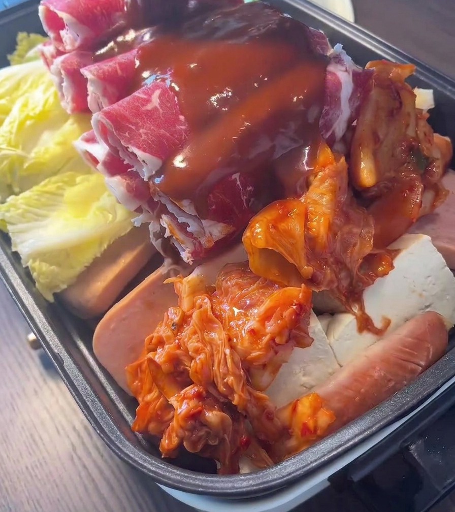 Una salsa de chile coreano roja y espesa que se rocía sobre una olla con capas de carne, kimchi y verduras.