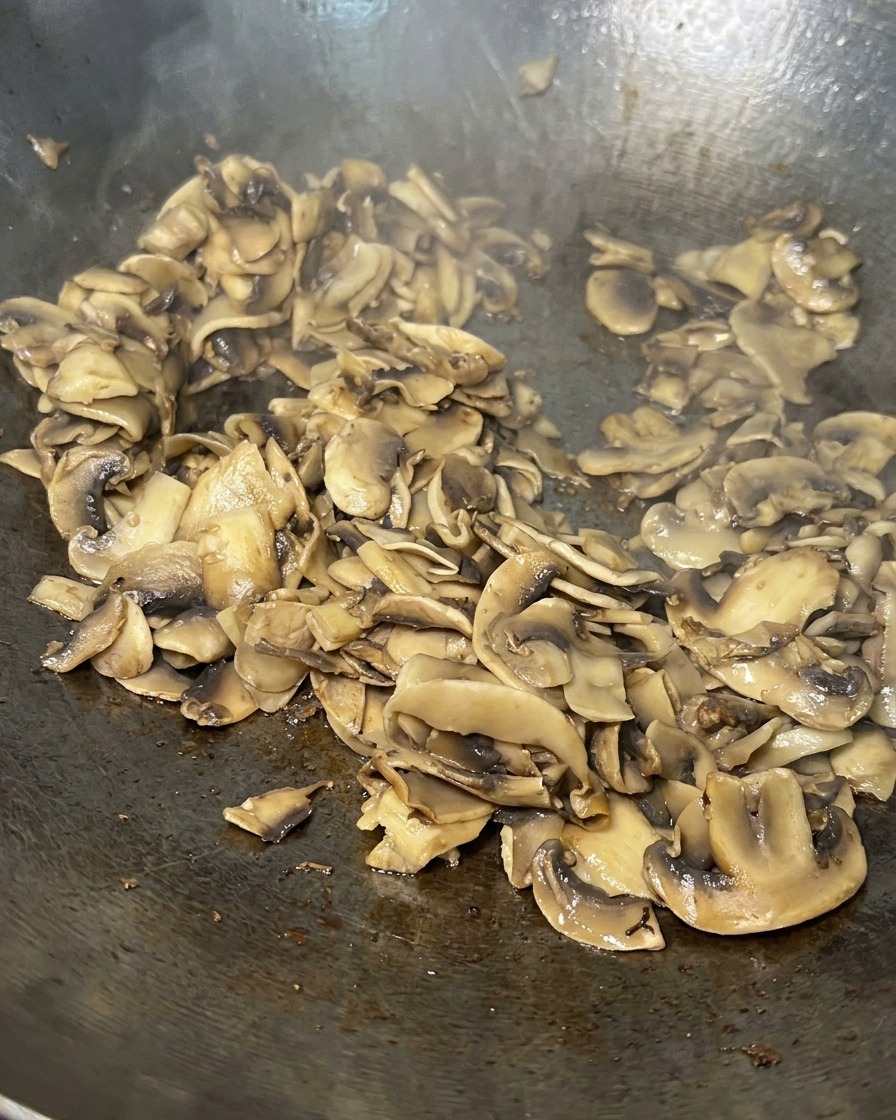 Láminas de champiñones salteadas en una sartén, cocinadas hasta quedar doradas y prácticamente secas.