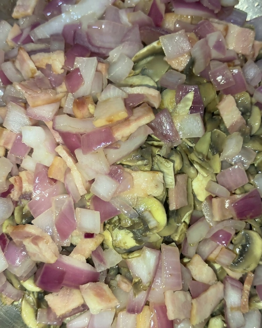 Combinación de champiñones dorados, cebolla morada translúcida y trocitos de bacon cocinados salteándose a la vez.