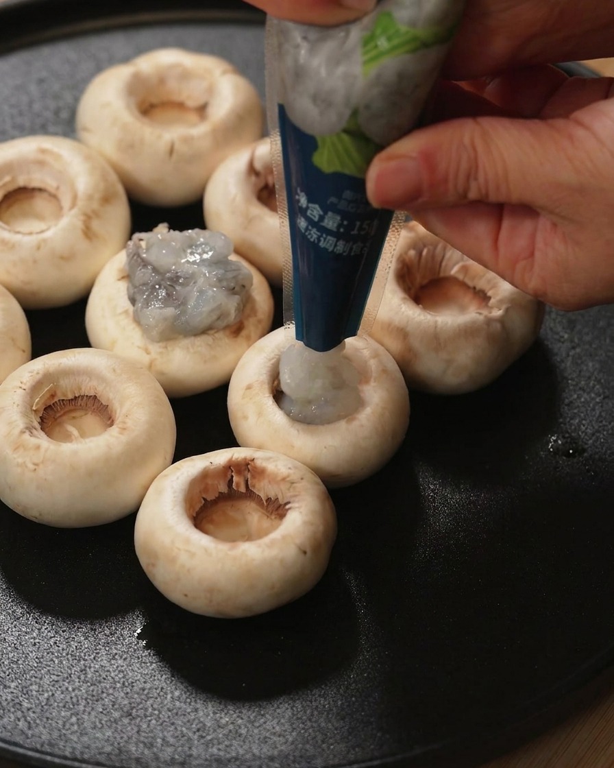 Una mano rellenando el interior de un sombrero de champiñón fresco con pasta de camarón cruda