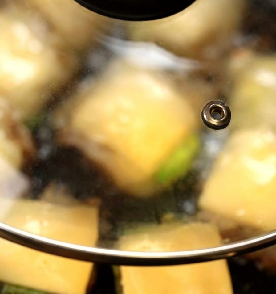 Una tapa de vidrio cubriendo la sartén donde las lonchas de queso empiezan a derretirse sobre las hamburguesas de champiñón