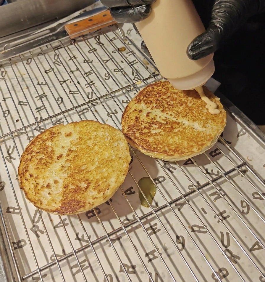 Salsa cremosa de color naranja saliendo de una botella de plástico sobre las dos mitades de pan tostado apoyadas en una rejilla.