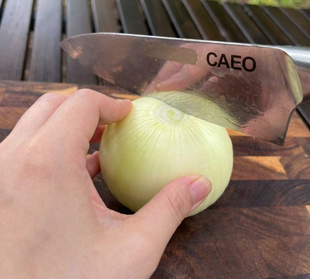 Una mano sostiene una cebolla blanca sobre una tabla de madera mientras un cuchillo de chef la rebana.