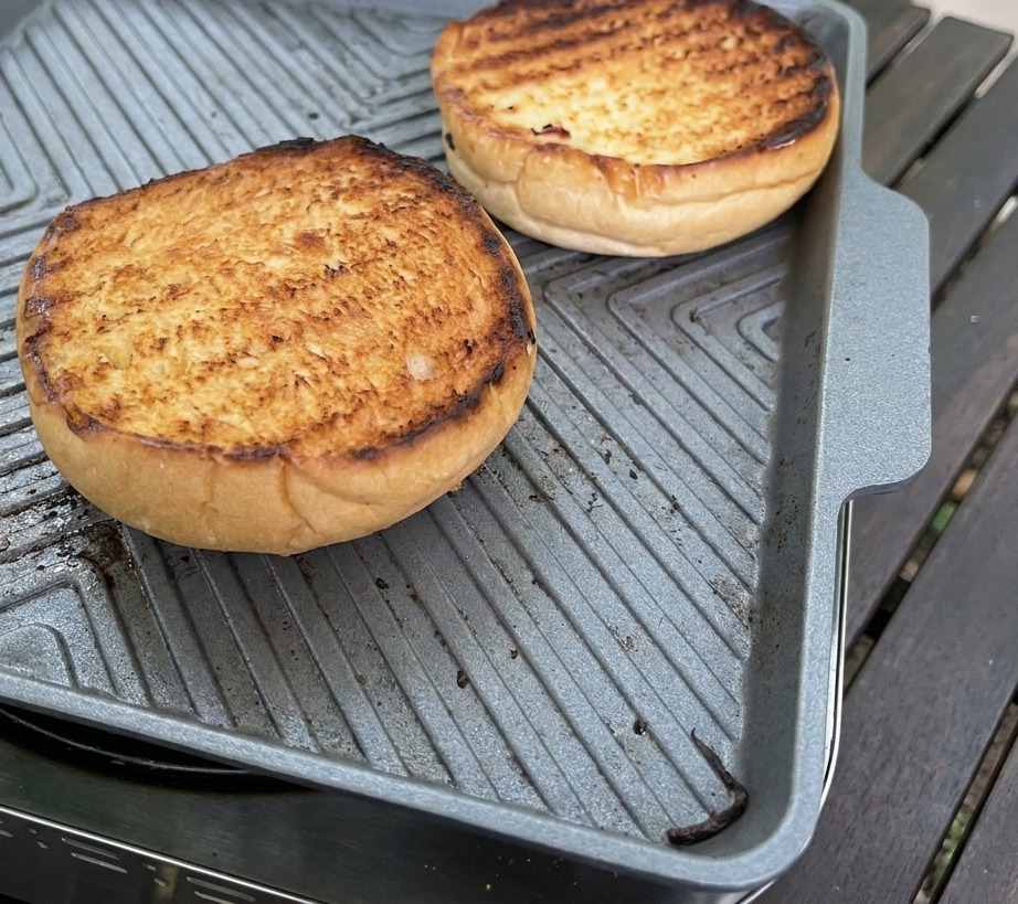 Una cuchara plateada untando una salsa rosa cremosa y espesa sobre la superficie dorada de un pan brioche tostado.