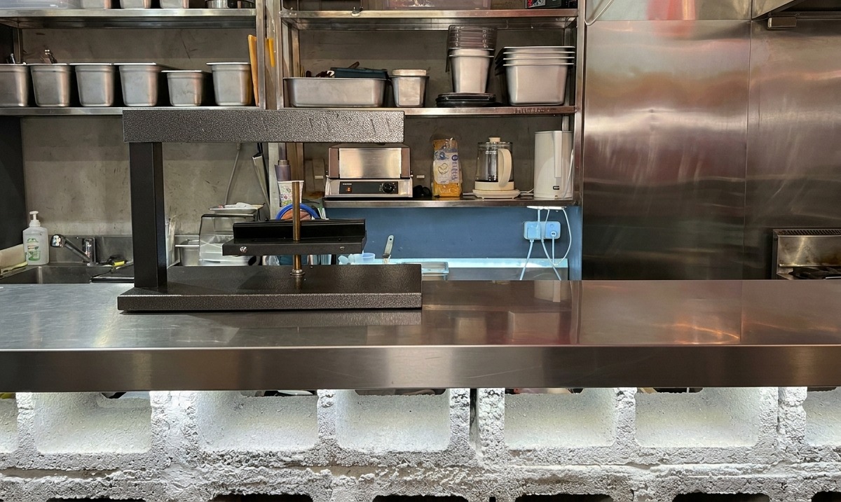 Un calentador eléctrico negro para queso raclette listo sobre una encimera de cocina de acero inoxidable.
