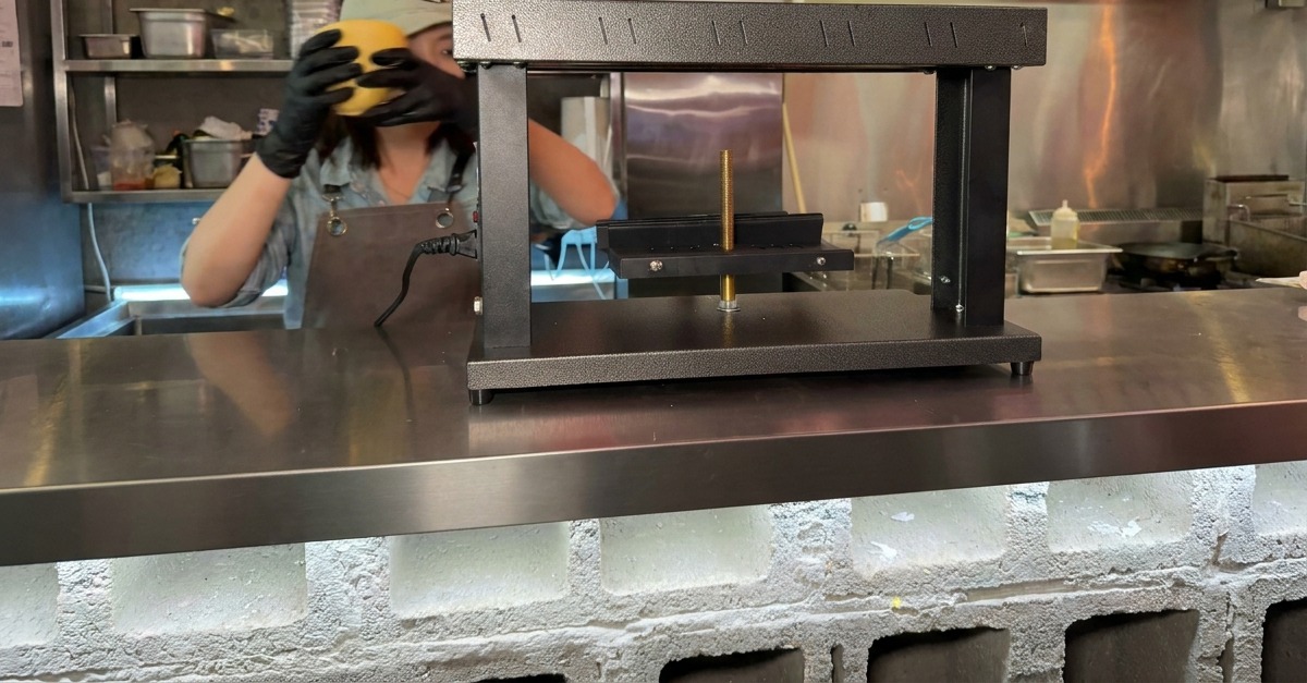 Manos colocando un bloque semicircular de queso en la base de una máquina especializada para fundir.