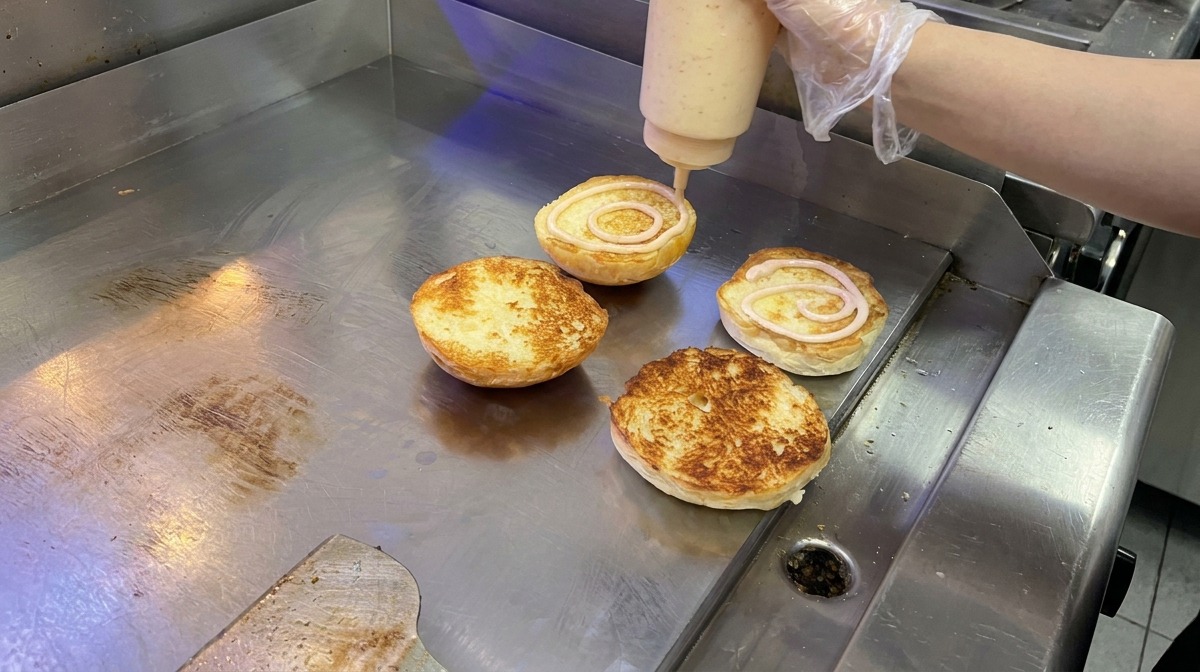Salsa rosada cremosa aplicándose en forma de espiral sobre panes brioche tostados en una plancha.