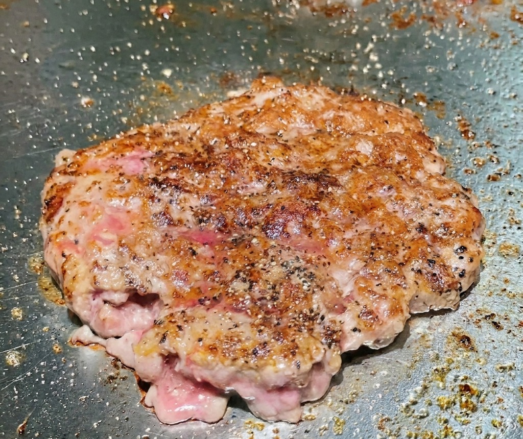 Una carne de res volteada en la plancha que muestra una superficie crujiente profundamente sellada y dorada.