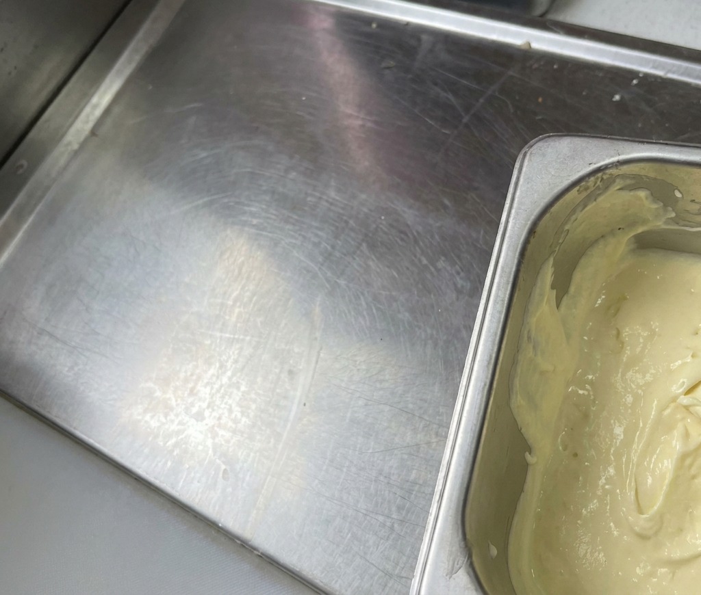Un recipiente de metal lleno con una salsa mezclada espesa de color amarillo pálido y apariencia suave y cremosa.
