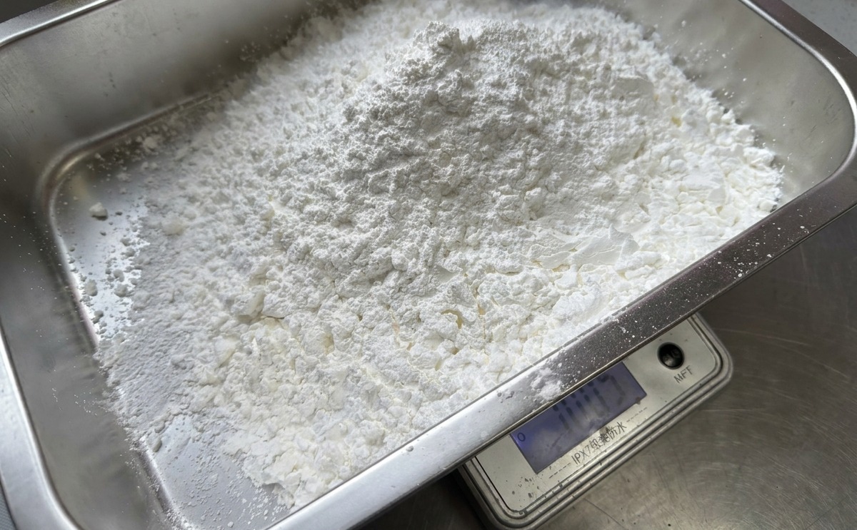 Una gran pila de almidón de maíz blanco pesándose en una báscula digital dentro de una bandeja rectangular de acero inoxidable.