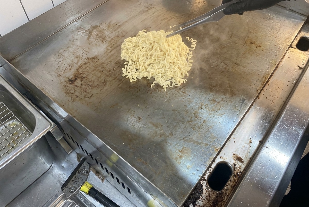 Vista de fideos humeantes y mantequilla derritiéndose sobre una gran superficie plana de metal para cocinar.