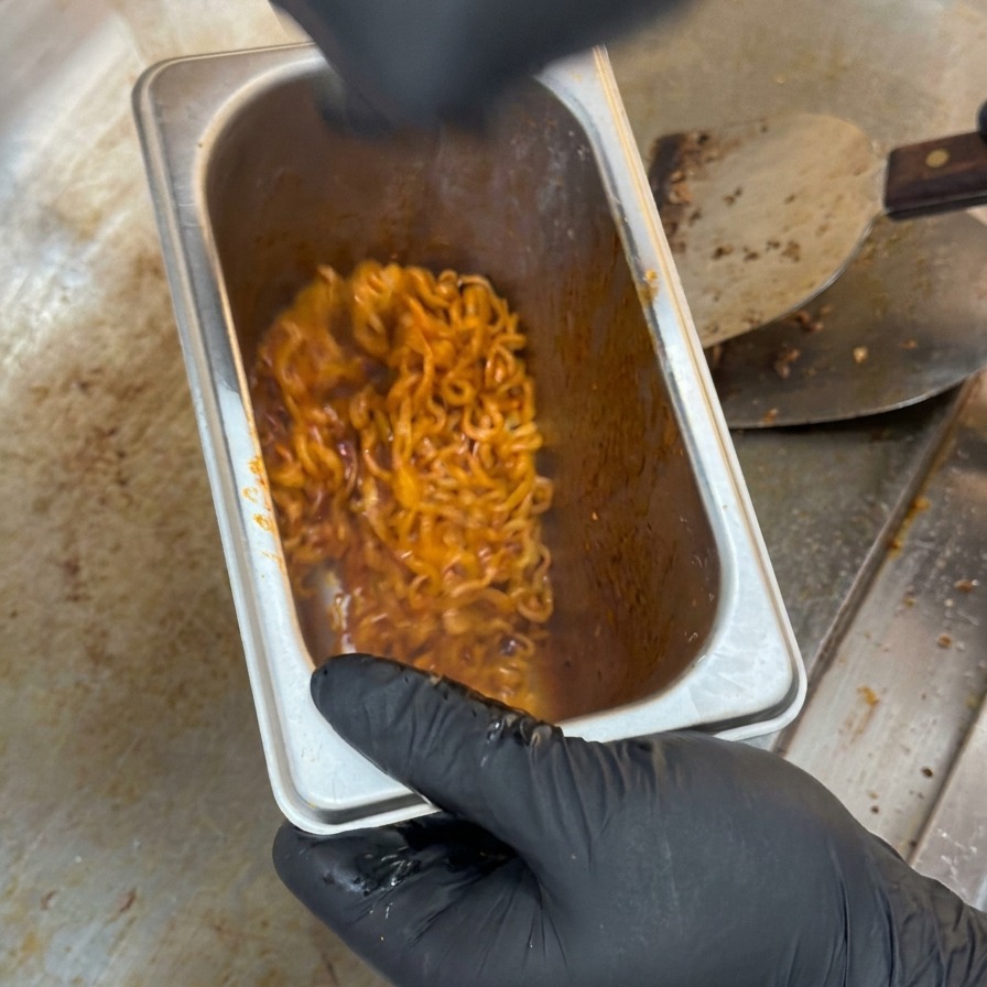 Fideos rojos picantes mezclándose y removiéndose dentro de un recipiente hondo de cocina de acero inoxidable.