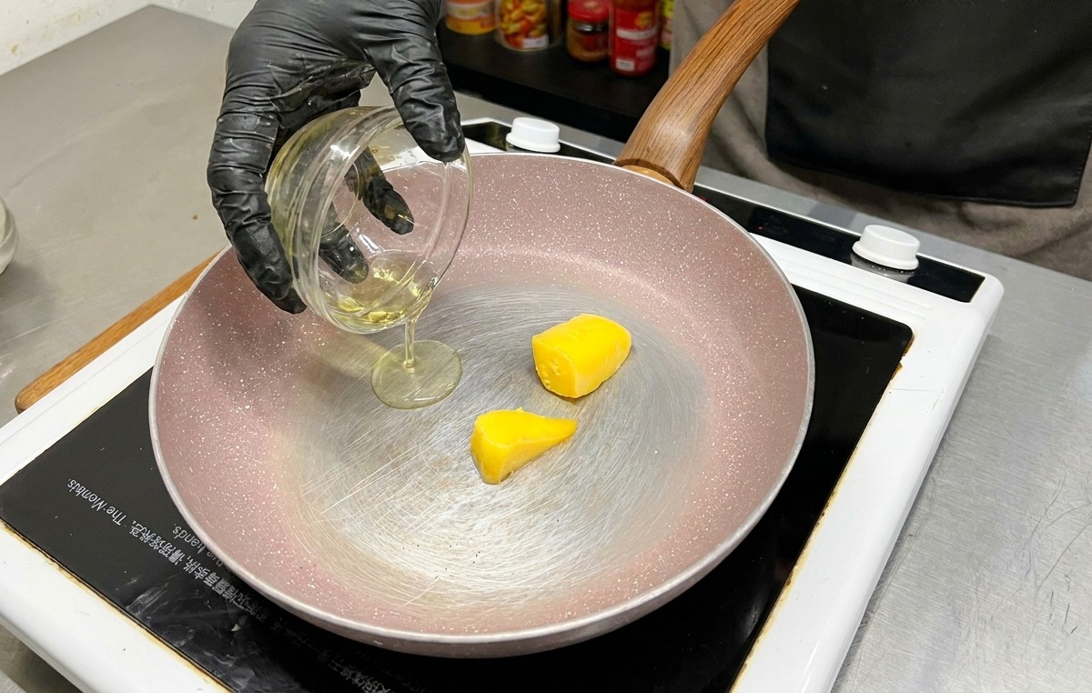 Dos cubos de mantequilla amarilla en una sartén mientras se vierte aceite de oliva desde un tazón de vidrio.