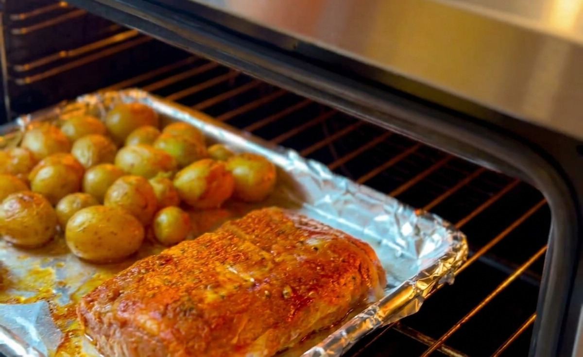 Una bandeja de horno con las costillas sazonadas con hierbas y patatas amarillas pequeñas se introduce en un horno precalentado para asarse.