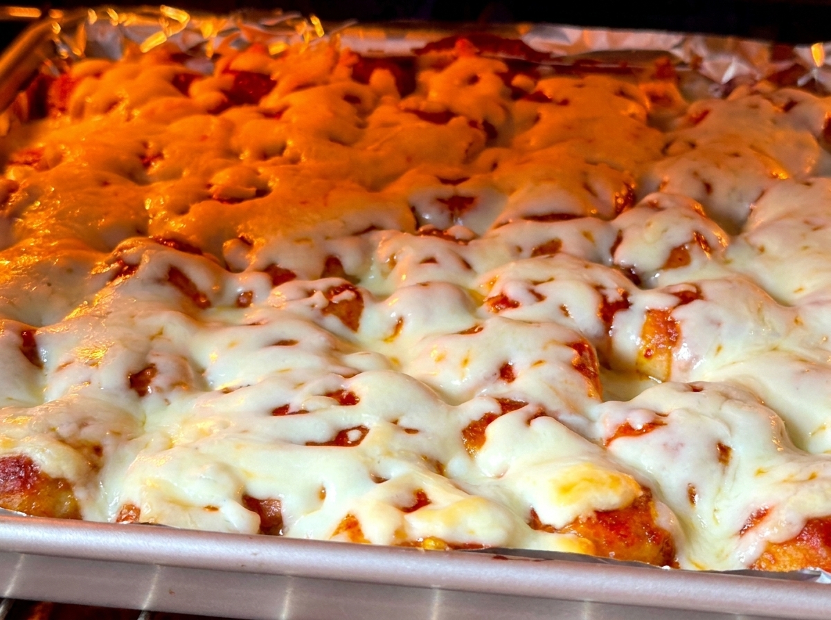 Vista de cerca de queso blanco espeso burbujeando y dorándose sobre la comida dentro de un horno encendido.