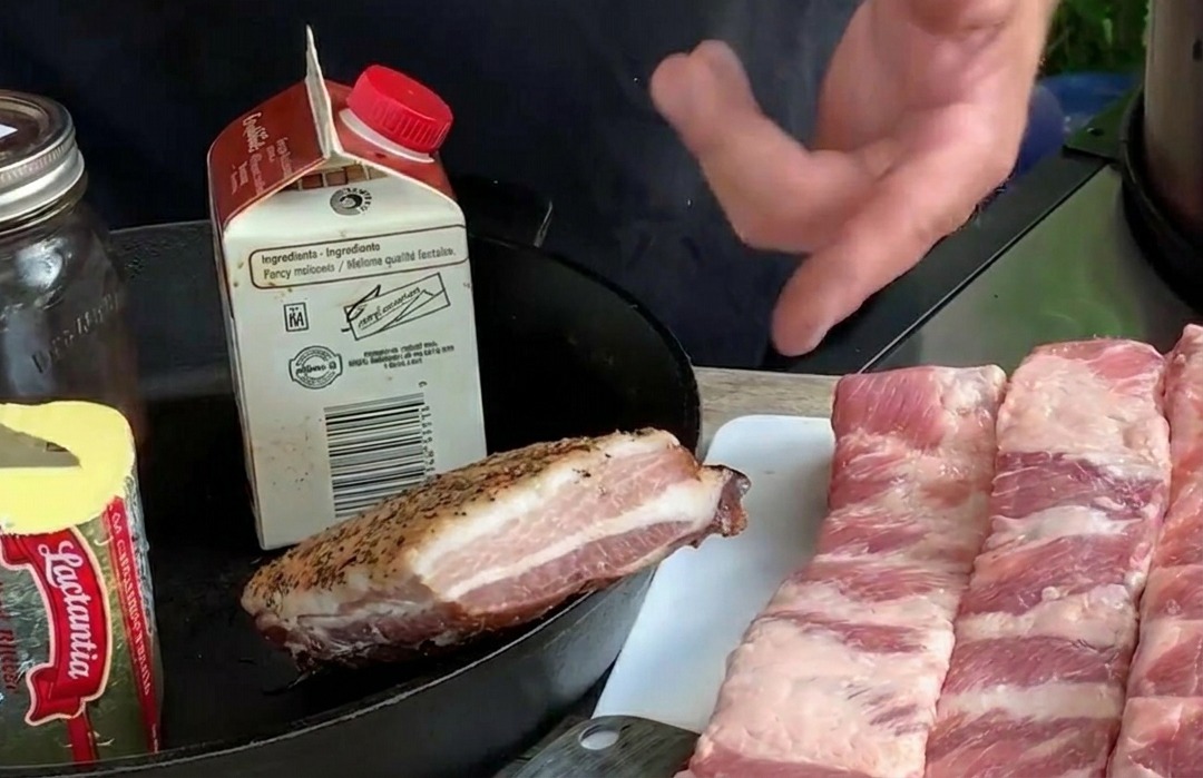 Varias tiras largas de costilla de cerdo cruda dispuestas sobre una tabla de picar blanca junto a ingredientes como mantequilla y arándanos frescos.
