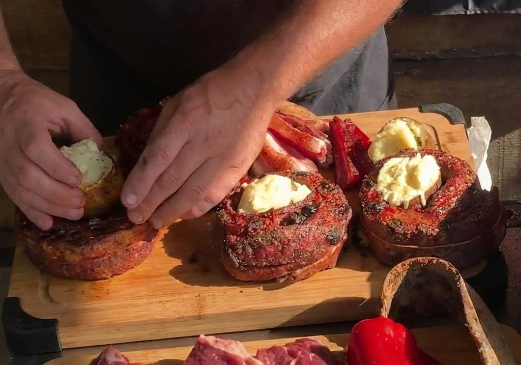 Manos colocando una papa asada entera en el centro hueco de una tira de costilla circular cocida sobre una tabla de madera.