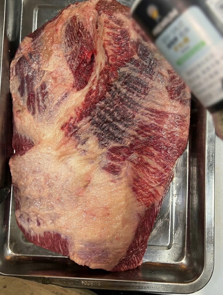Sal marina gruesa espolvoreada sobre una pieza grande de brisket crudo en una bandeja de acero inoxidable.