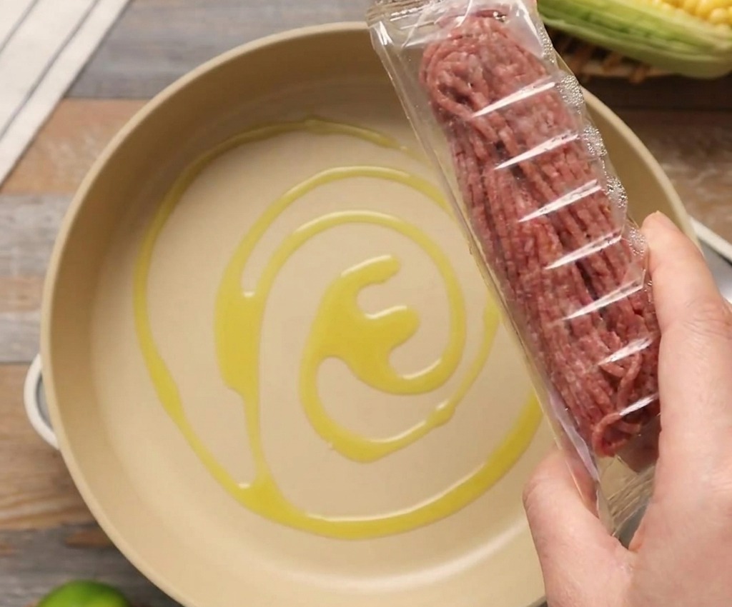 Un paquete de carne molida cruda sostenido sobre una sartén con un toque de aceite de oliva.