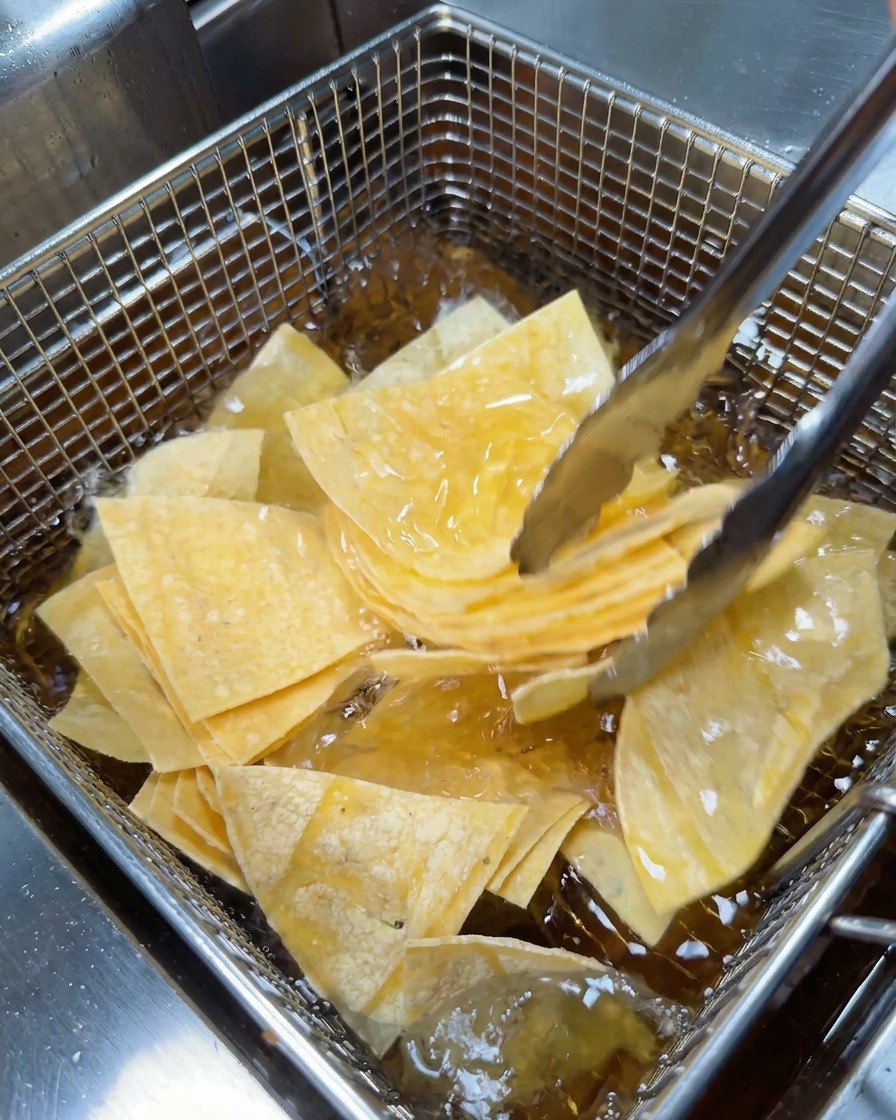 Unas pinzas metálicas colocando triángulos de tortilla en una canasta para freír.