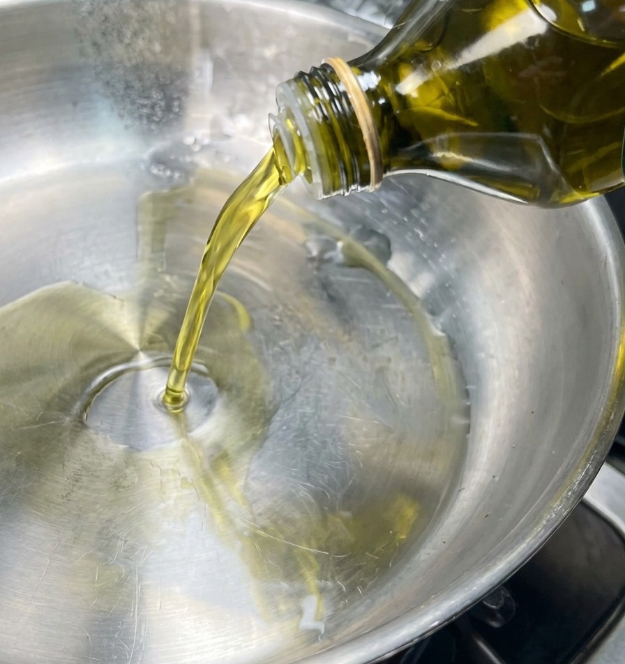 Un chorro de aceite de oliva vertiéndose en una sartén de acero inoxidable.