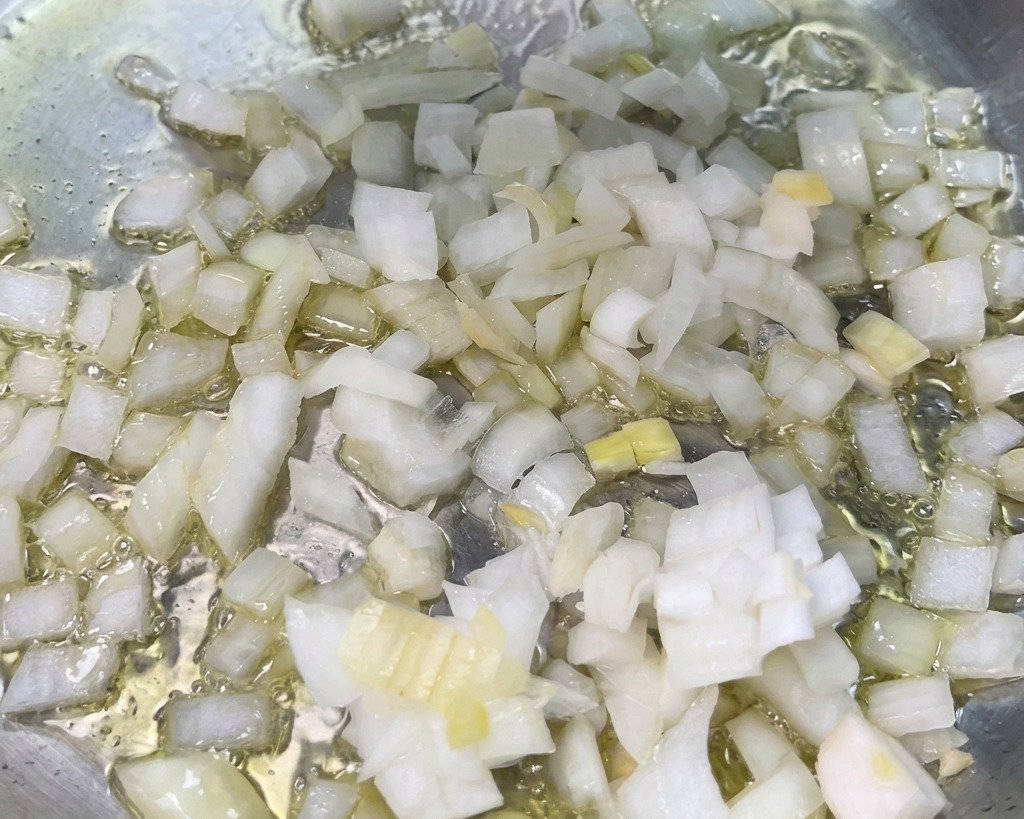 Cebolla blanca en cubos sofriéndose en aceite caliente en una sartén.