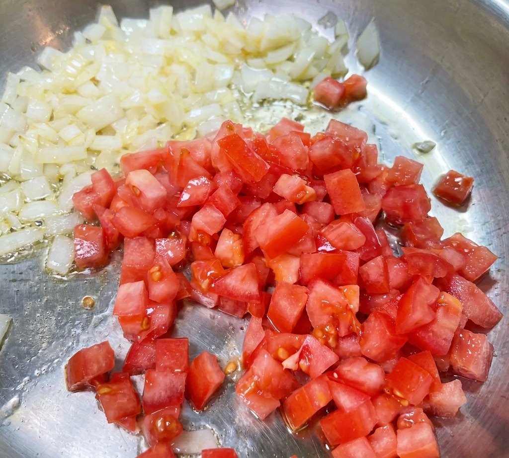 Tomates rojos picados mezclándose con cebolla sofrita en una sartén.