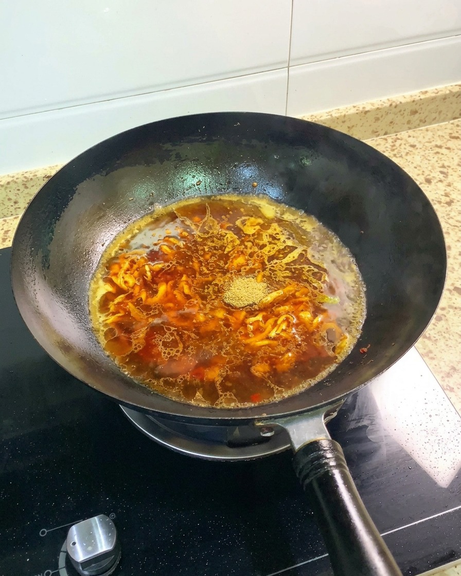 Polvo de cinco especias chinas y un anís estrellado entero reposando sobre el caldo marrón rojizo en un wok negro.