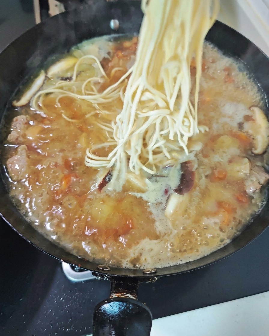 Un manojo de fideos frescos cayendo en un wok burbujeante de sabrosa sopa de pollo con láminas de setas.