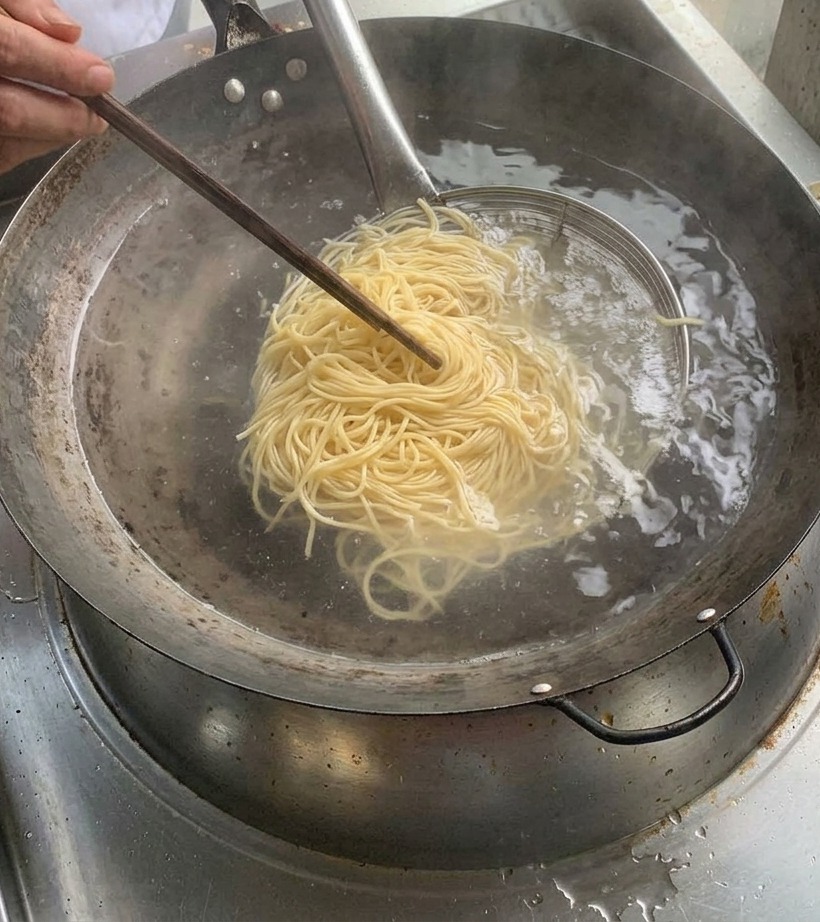 Fideos cocidos sostenidos en un colador metálico sobre una olla de agua hirviendo.