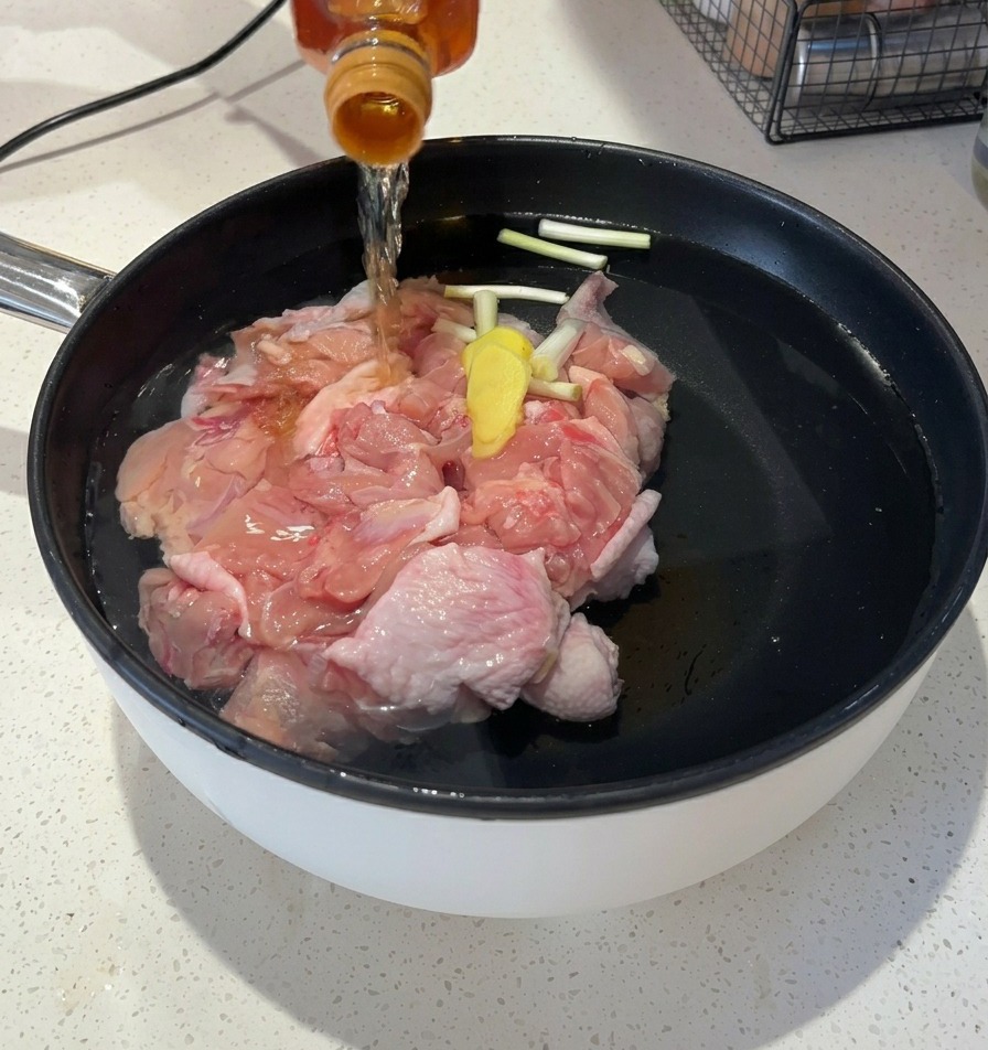 Vertiendo un líquido ámbar transparente desde una botella de vidrio a la olla con agua y pollo.