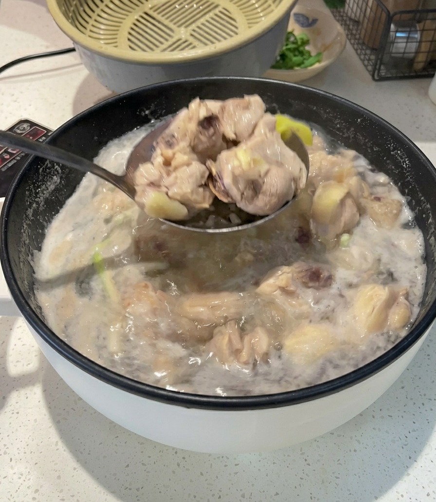 Un cucharón de metal sacando trozos de pollo blanqueado y opaco de una olla con agua hirviendo y espumosa.
