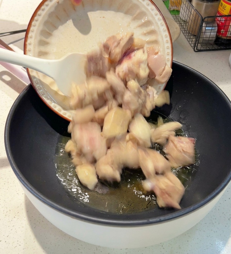 Un plato blanco volcando los trozos de pollo blanqueado en una sartén profunda con aceite caliente.