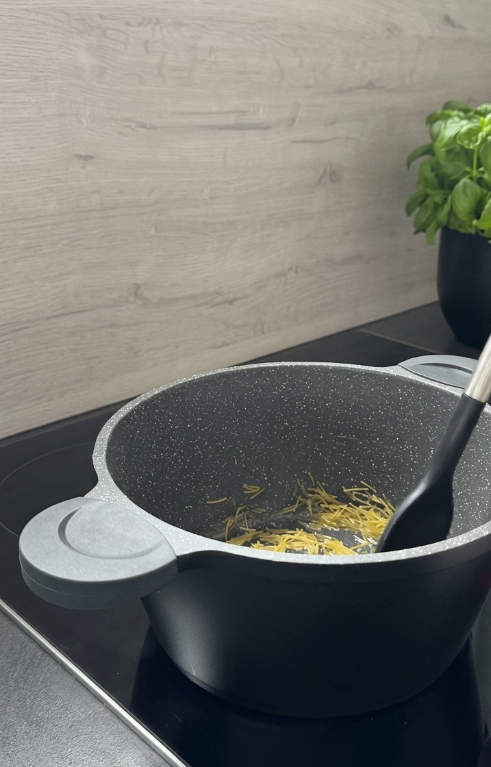 Pasta pequeña con forma de piñón siendo removida con una espátula negra en una olla gris mientras se dora.