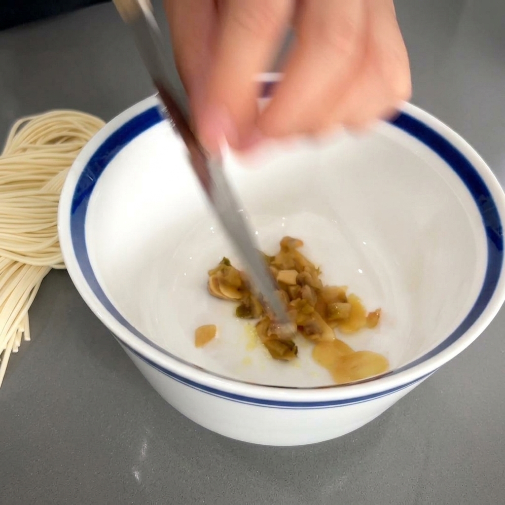 La hoja de un cuchillo deslizando verduras encurtidas picadas en un cuenco con ajo y sazonador.