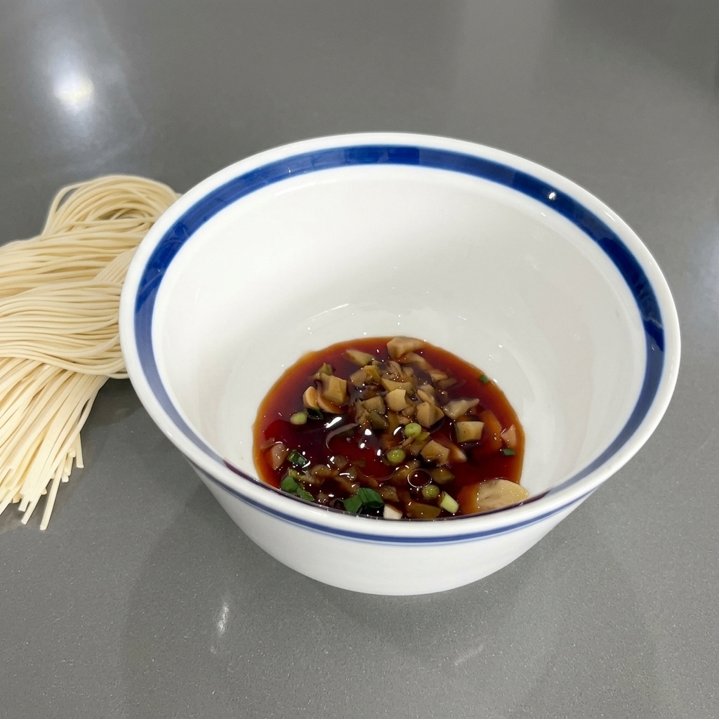 El cuenco con la salsa de soja y los condimentos mostrando un brillo ligero por el aceite de sésamo.