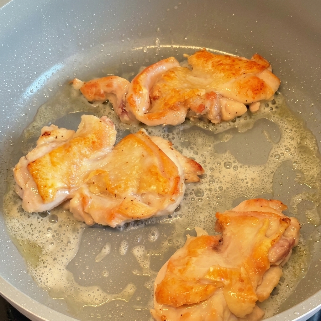 Tres contramuslos de pollo friéndose en una sartén, volteados para mostrar su piel dorada y crujiente.