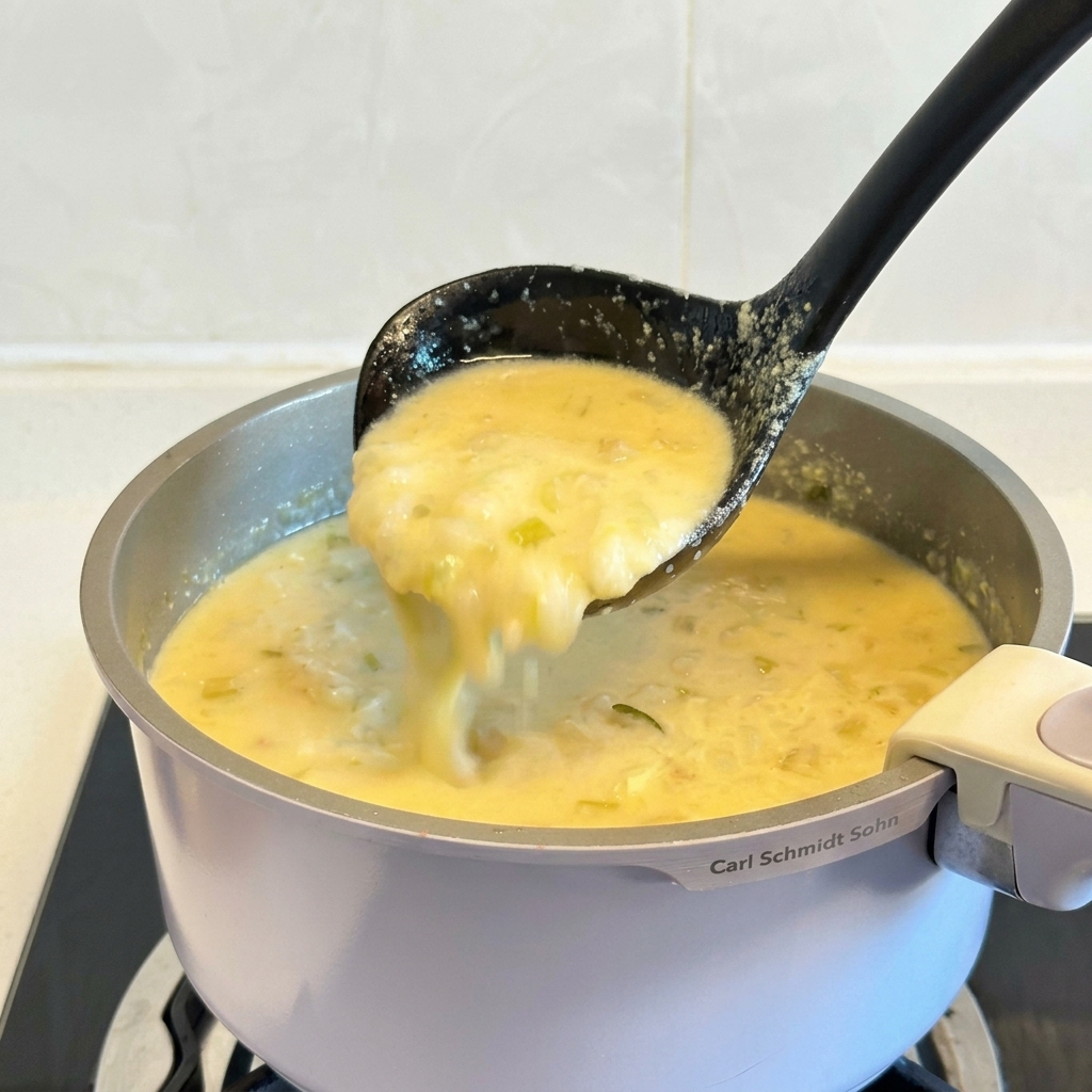 Un cucharón negro levantando una porción de sopa griega de pollo y limón, espesa y cremosa, desde una olla.