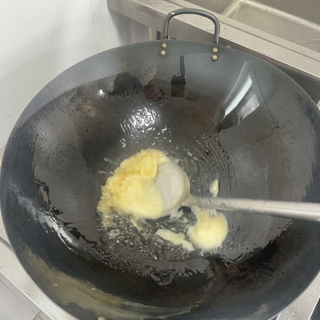 Un trozo sólido de manteca de cerdo blanca derritiéndose en un aceite transparente al fondo de un wok negro curado.