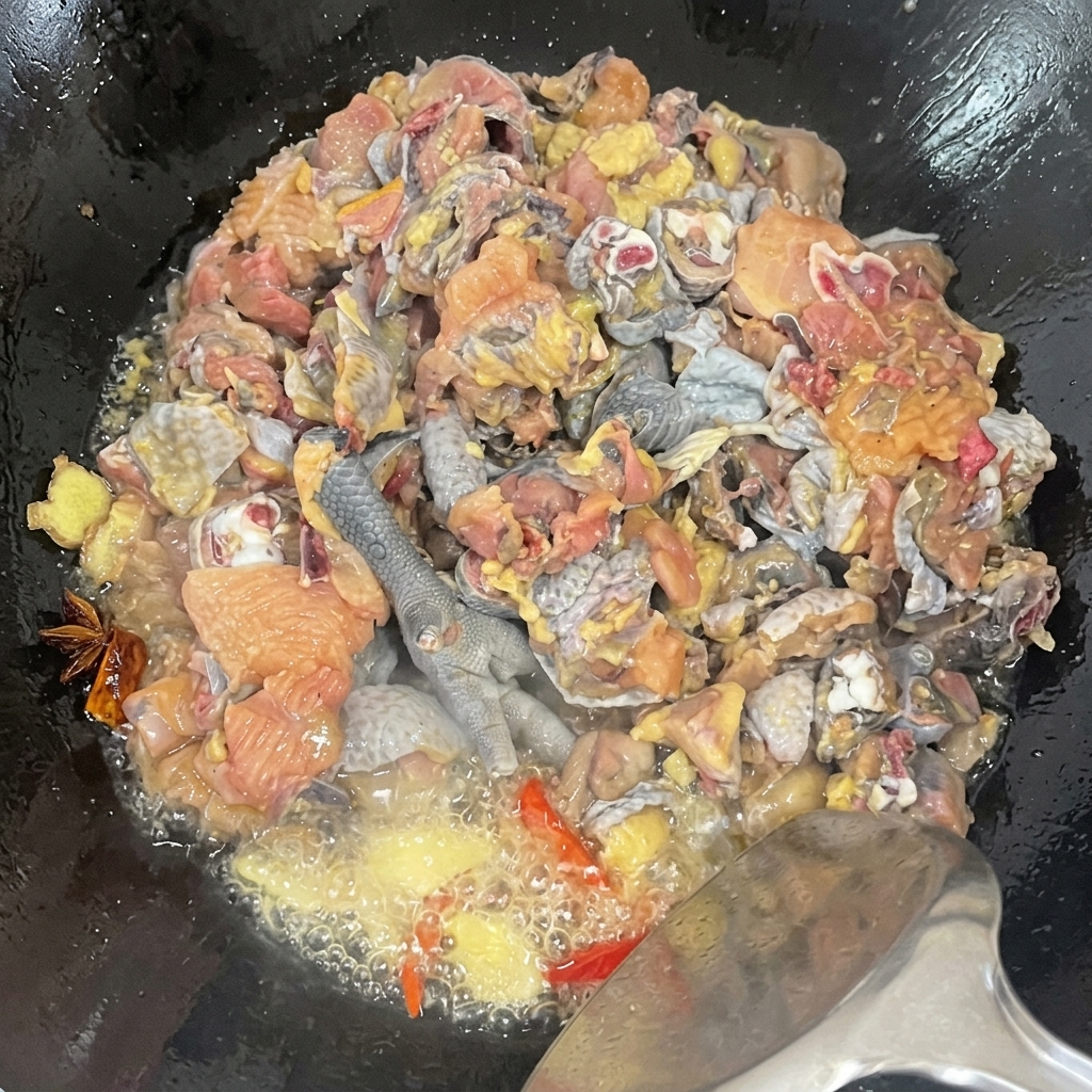 Primer plano de trozos de pollo silkie siendo salteados en un wok con especias, mostrando el aceite burbujeante y el proceso de sazonado.
