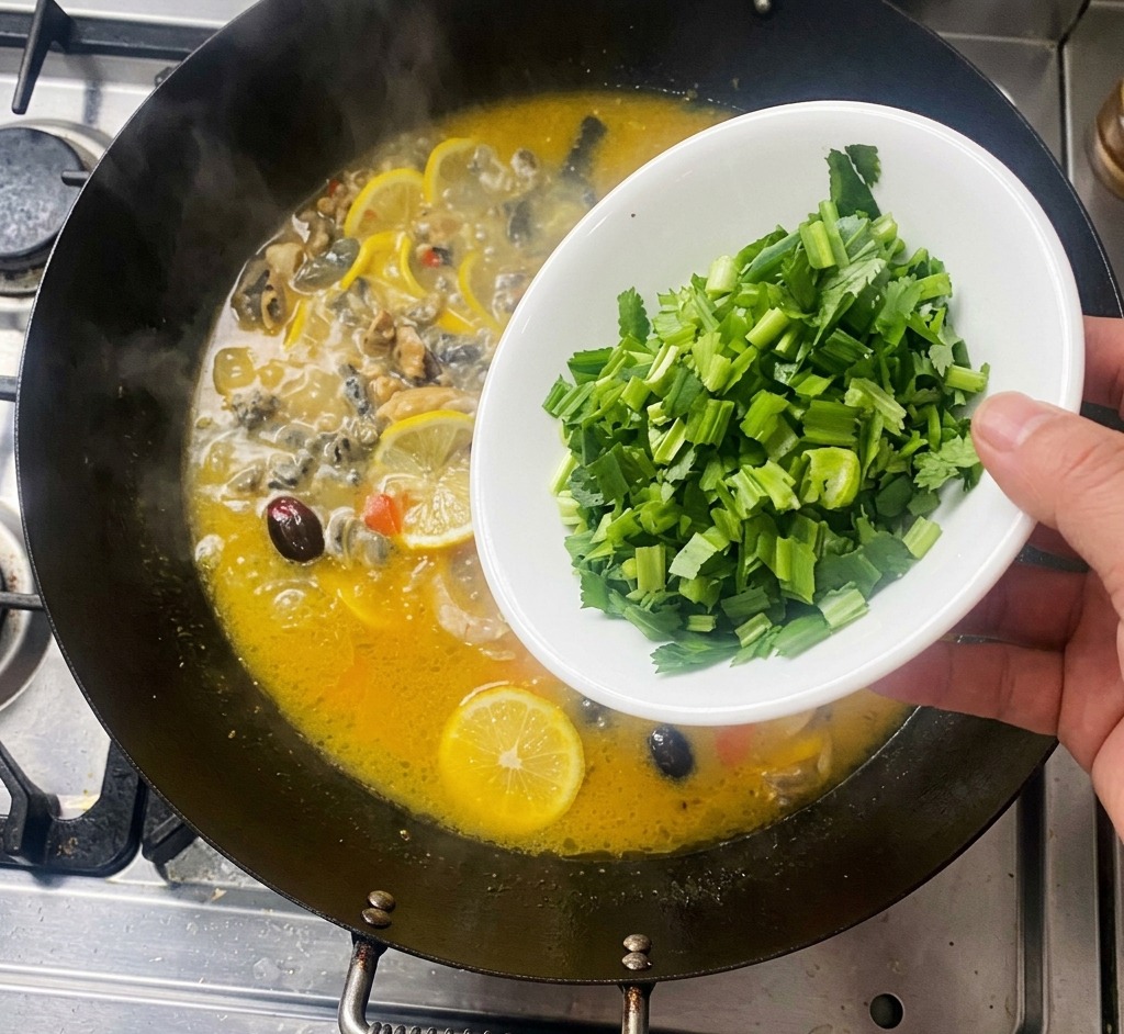 Una mano echando cilantro verde picado desde un cuenco blanco a un wok burbujeante con pollo y rodajas de limón.