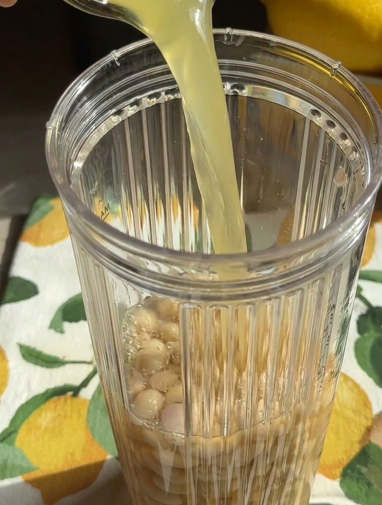 Un líquido amarillento se vierte desde un vaso en la jarra de la batidora llena de alubias blancas enteras.