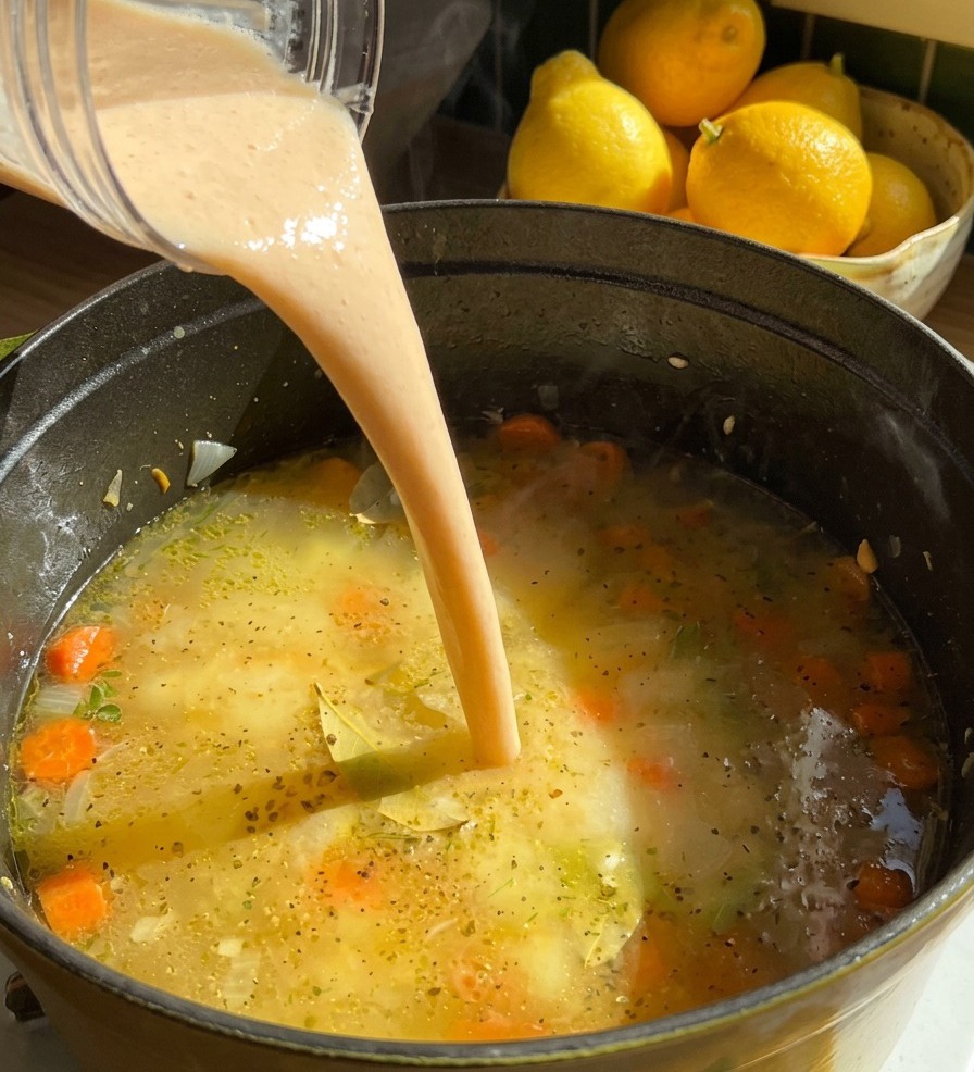 Un chorro de puré de alubias espeso y de color crema se vierte desde el vaso de la batidora en una olla de sopa hirviendo con rodajas de zanahoria.