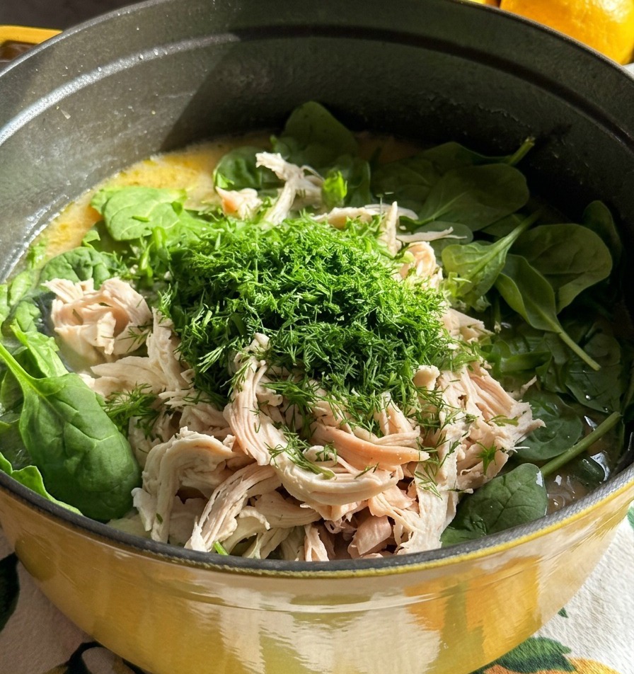 Una olla de sopa coronada con carne de pollo blanca desmenuzada y un gran montón de eneldo verde fresco finamente picado.