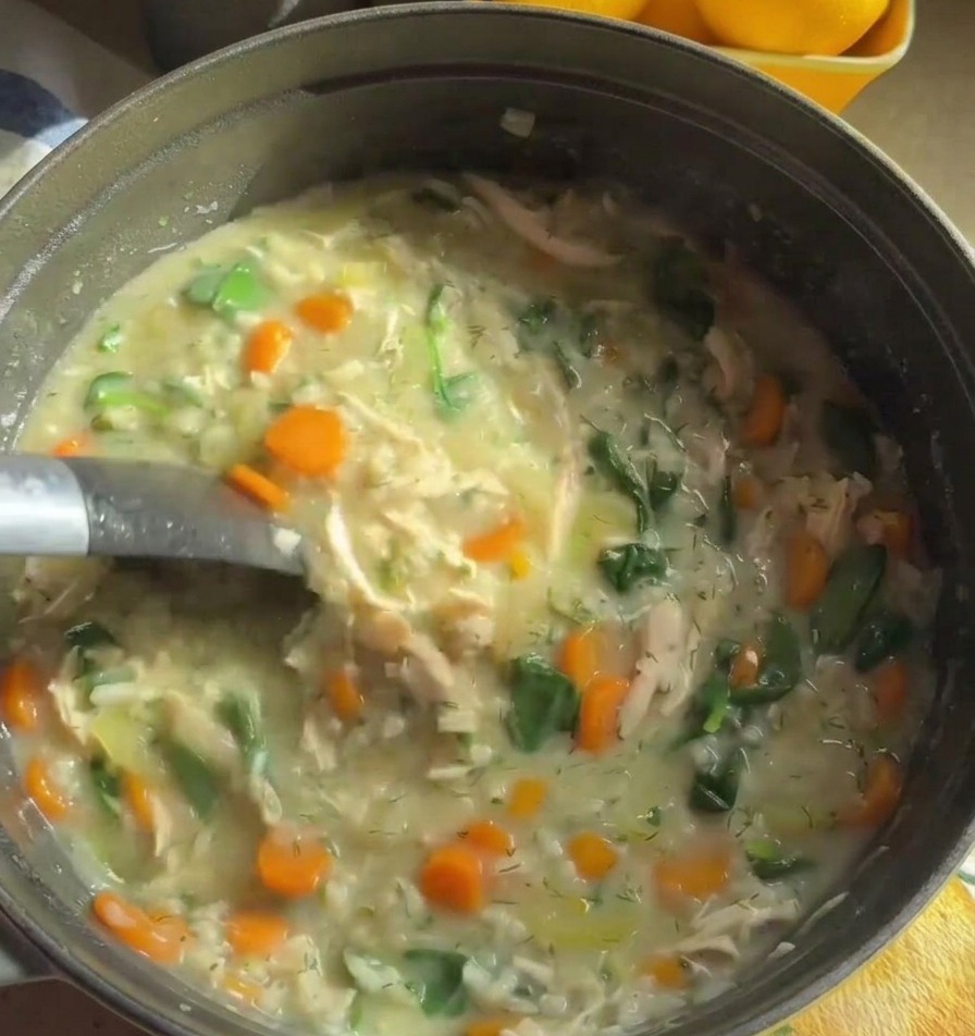 Un cucharón de metal remueve una sopa de pollo cremosa y espesa repleta de zanahorias naranjas y espinacas verdes.